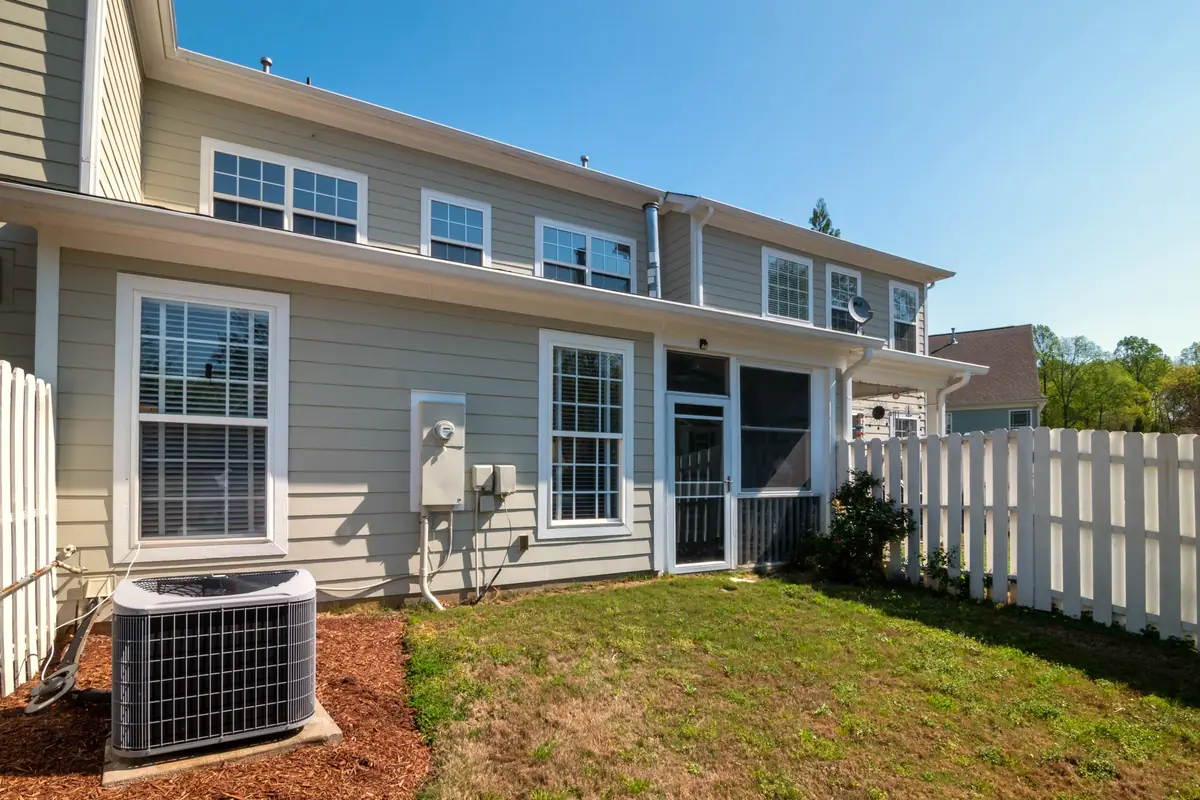 Central air condenser beside a two-story house with a white fence and green lawn