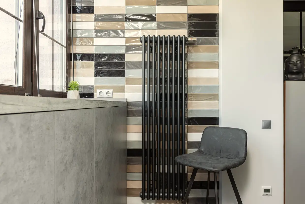 Black column radiator against a tiled wall